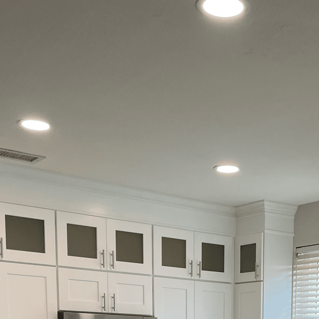 A kitchen with white cabinets and lights on the ceiling.